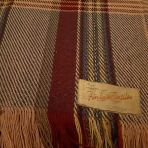 Peut inclure: Une couverture tiss&eacute;e avec un motif &agrave; carreaux dans les tons de rouge, bleu, jaune et beige. La couverture a un bord &agrave; franges et une &eacute;tiquette qui indique "Finlay Textiles".