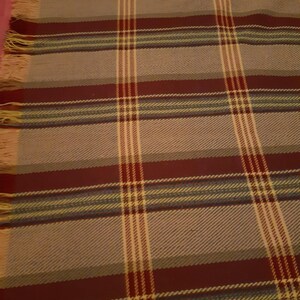 Peut inclure: Une couverture rectangulaire &agrave; motif &eacute;cossais. La couverture pr&eacute;sente une base grise avec des rayures bordeaux, cr&egrave;me et sarcelle. Les bords ont une frange de couleur jaune clair. La couverture est faite d'un mat&eacute;riau tiss&eacute;.