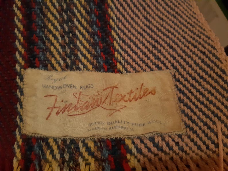 Peut inclure: Textile tiss&eacute; avec une &eacute;tiquette indiquant "Royal Handwoven Rugs Fintan Textiles Super Quality Pure Wool Made in Australia". Le textile pr&eacute;sente un motif de fils rouges, bleus, jaunes et bruns.