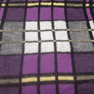 May include: A close-up of a purple, black, white, and grey plaid blanket. The blanket has a repeating pattern of squares and rectangles. The colours are vibrant and the texture appears soft.