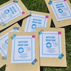 Puede incluir: Cinco sobres de papel marrón con un diseño impreso en blanco. Cada sobre tiene un personaje de dibujos animados azul con orejas de elfo y un bocadillo que dice "Mystery Grab Bag". El texto dentro del bocadillo dice "Inside you'll find: 1 Small Print, 1 Oopsie Bookmark, 2 Stickers". Cada sobre tiene una etiqueta de precio rosa que dice "8 €".
