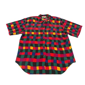 May include: A short-sleeved button-down shirt with a vibrant checkerboard pattern. The design features squares of red, green, yellow, purple, and blue, separated by black lines. The shirt has a collar and is buttoned down the front.