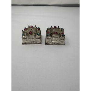 Könnte beinhalten: Zwei silberfarbene Miniatur-Taj-Mahal-Skulpturen. Jede hat ein detailliertes architektonisches Design mit roten und grünen Akzenten auf den Kuppeln. Die Skulpturen stehen nebeneinander.
