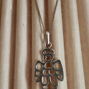 Puede incluir: Collar con colgante de plata con dise&ntilde;o de &aacute;ngel. El colgante, una silueta calada de &aacute;ngel con halo, cuelga de una fina cadena. El fondo es de tela beige. Marcado con '4 KICK 925'.