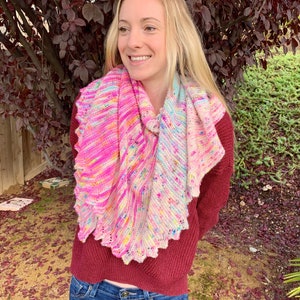 May include: A woman wearing a pink, white, and blue crocheted shawl with a scalloped edge. She is wearing a maroon sweater and blue jeans.