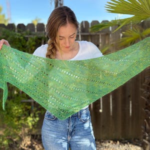 May include: A green and yellow knitted shawl with a triangular shape. The shawl has a delicate, openwork design with a textured appearance. The color is a vibrant mix of greens and yellows, creating a visually appealing accessory.