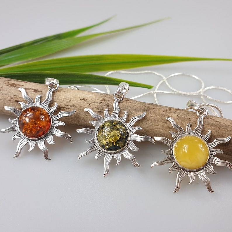 Three silver sun pendant necklaces with amber stones. The stones are different colours: orange, green, and yellow.