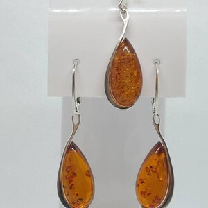 May include: A silver teardrop pendant necklace and matching earrings set with amber stones. The pendant and earrings have a simple, elegant design.