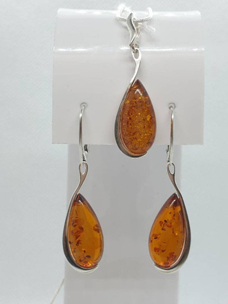 May include: A silver teardrop pendant necklace and matching earrings set with amber stones. The pendant and earrings have a simple, elegant design.