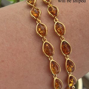 May include: A gold chain bracelet with amber teardrop-shaped stones. The bracelet is shown on a person's wrist.