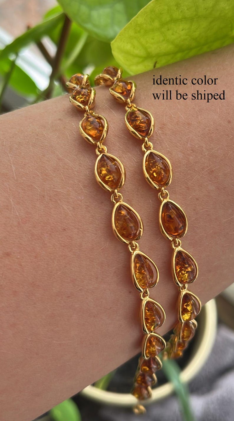 May include: A gold chain bracelet with amber teardrop-shaped stones. The bracelet is shown on a person's wrist.
