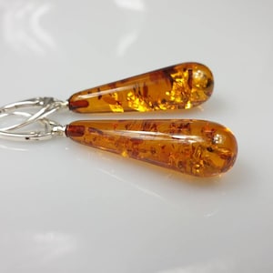 May include: A pair of silver dangle earrings with amber teardrop-shaped stones. The amber is a warm, honey colour with inclusions.