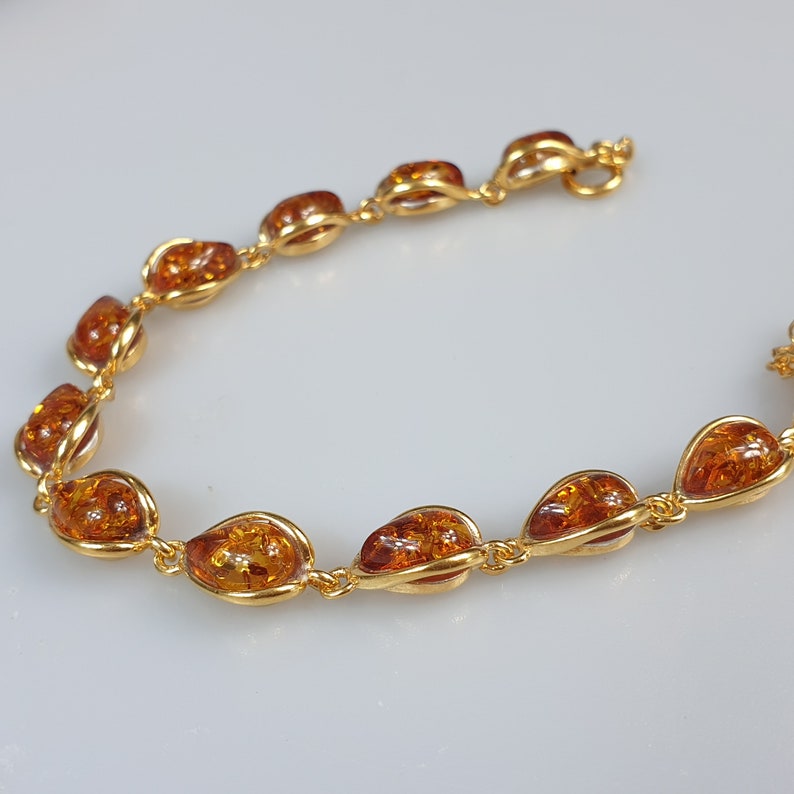 May include: A gold bracelet with amber-colored stones. The bracelet is made of a delicate chain with oval-shaped stones.