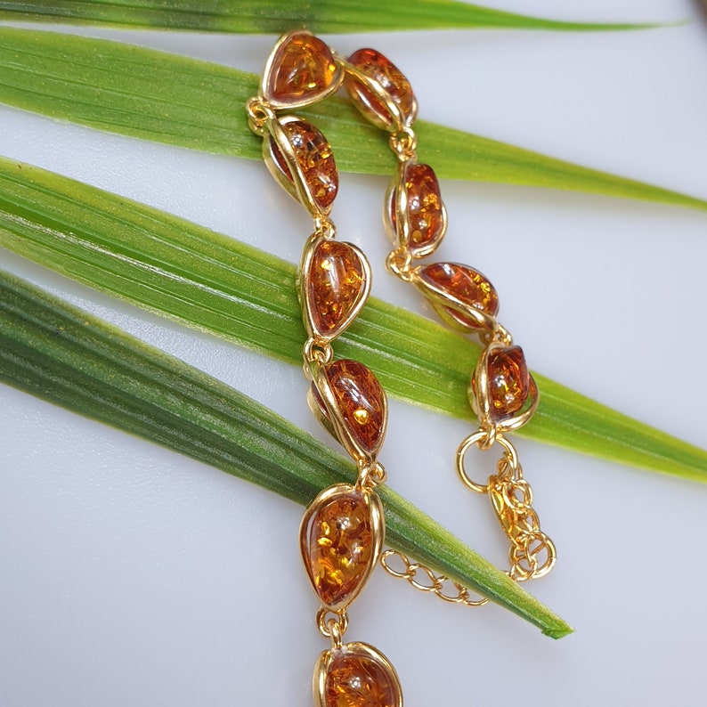 May include: A gold bracelet with amber teardrop-shaped stones. The bracelet is on a green leaf background.