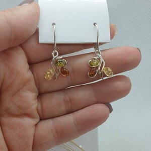 Op de afbeelding: Zilveren oorhangers met amberstenen in tinten geel, oranje en bruin. De oorhangers hebben een delicaat, gebogen ontwerp.