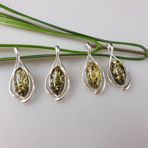 May include: Four silver pendants with green amber stones. Each pendant features a teardrop-shaped design with a delicate swirl.