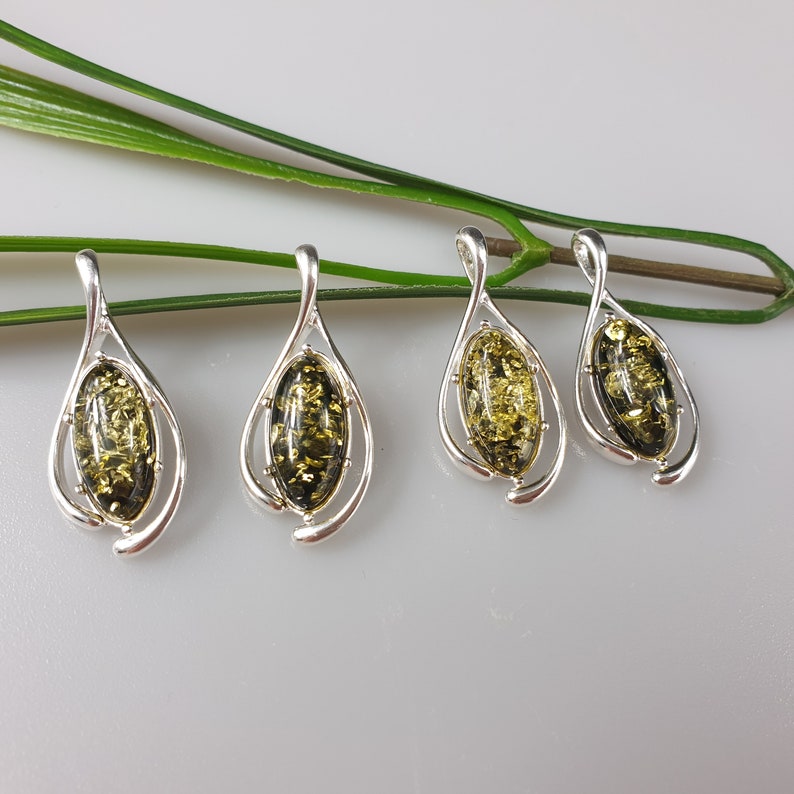 May include: Four silver pendants with green amber stones. Each pendant features a teardrop-shaped design with a delicate swirl.