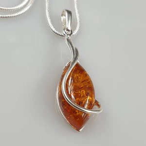 May include: A silver chain necklace with a pendant featuring a teardrop-shaped amber stone wrapped in silver wire.