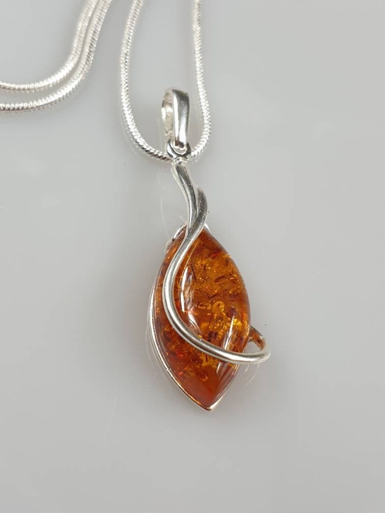 May include: A silver chain necklace with a pendant featuring a teardrop-shaped amber stone wrapped in silver wire.