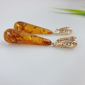 May include: A pair of amber drop earrings with gold filigree accents. The amber is a rich, warm brown colour with natural inclusions.