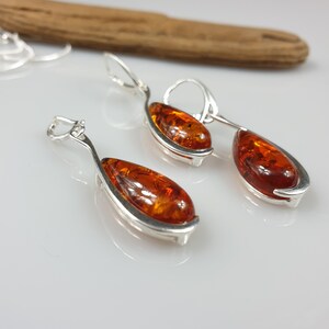 May include: A pair of silver dangle earrings with amber teardrop-shaped stones. The earrings have a curved design and are a classic style.