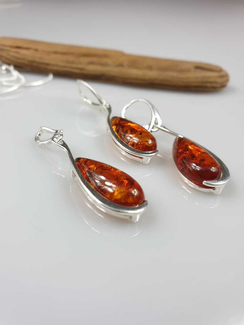 May include: A pair of silver dangle earrings with amber teardrop-shaped stones. The earrings have a curved design and are a classic style.