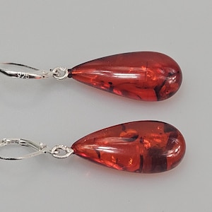 Peut inclure: Une paire de boucles d'oreilles en forme de goutte d'eau, de couleur rouge-orange intense. Les boucles d'oreilles ont une fermeture à levier argentée. Elles sont faites d'un matériau translucide.
