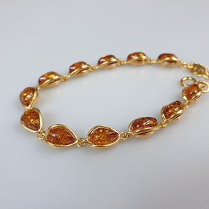May include: A gold bracelet with amber teardrop-shaped stones. The bracelet is made of a delicate chain and has a simple design.