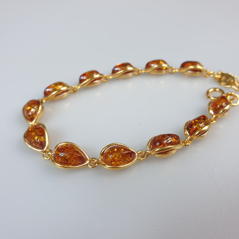 May include: A gold bracelet with amber teardrop-shaped stones. The bracelet is made of a delicate chain and has a simple design.