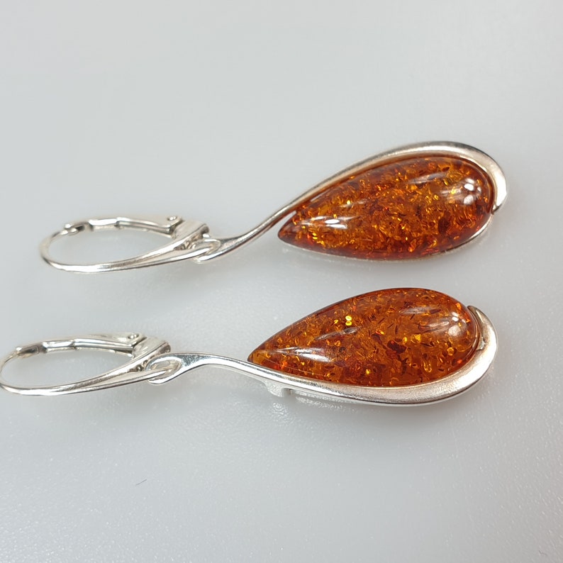 May include: A pair of silver dangle earrings with teardrop-shaped amber stones. The amber is a rich, warm brown color with flecks of gold.