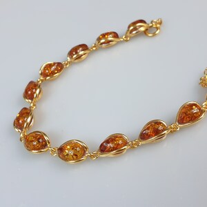 May include: A gold bracelet with amber stones. The stones are oval shaped and have a teardrop design. The bracelet has a lobster clasp.