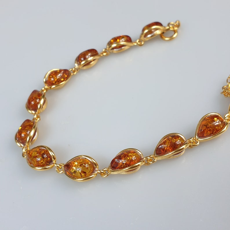May include: A gold bracelet with amber stones. The stones are oval shaped and have a teardrop design. The bracelet has a lobster clasp.