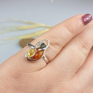 May include: A silver ring featuring three amber stones in a leaf-like design. The stones are yellow, orange, and green.