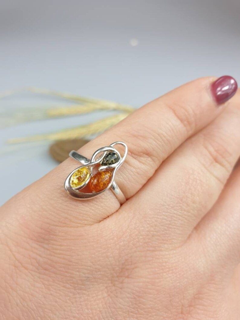 May include: A silver ring featuring three amber stones in a leaf-like design. The stones are yellow, orange, and green.