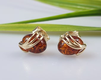 May include: A pair of gold earrings with amber stones. The stones are oval shaped and set in a delicate gold cage design.