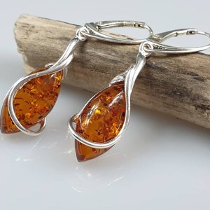 May include: A pair of silver dangle earrings with amber teardrop-shaped stones. The earrings are twisted and have a delicate design.
