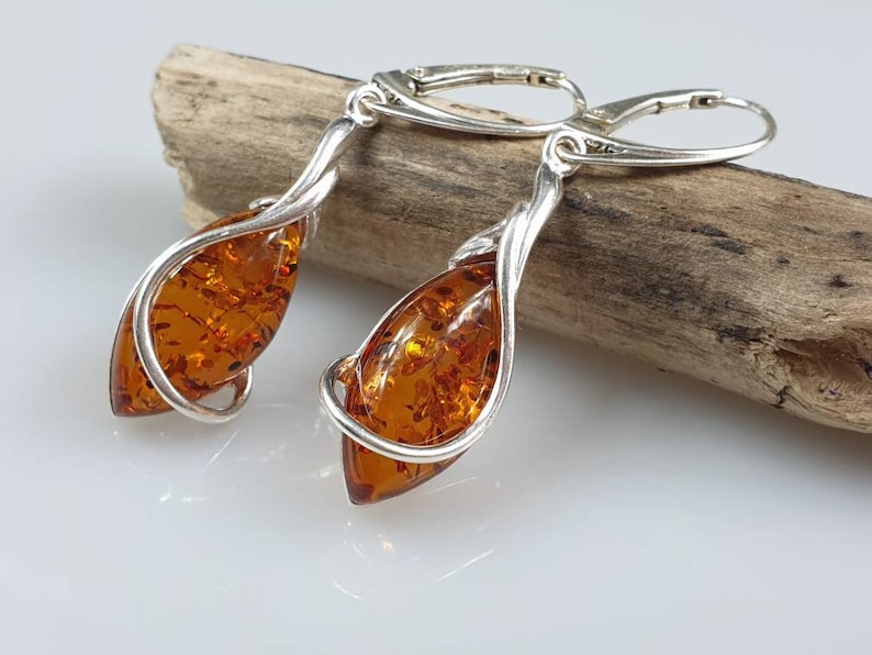 May include: A pair of silver dangle earrings with amber teardrop-shaped stones. The earrings are twisted and have a delicate design.