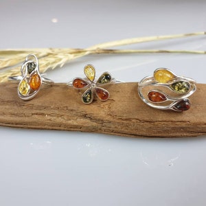 May include: Three silver rings with amber stones. The rings feature different designs, including a flower, a swirl, and a vine.
