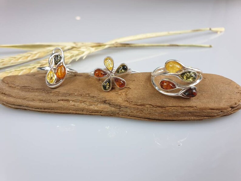 May include: Three silver rings with amber stones. The rings feature different designs, including a flower, a swirl, and a vine.