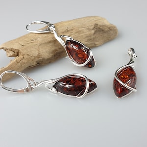 May include: A set of amber earrings and a pendant with silver wire wrapped around the amber stones. The earrings have silver hooks.