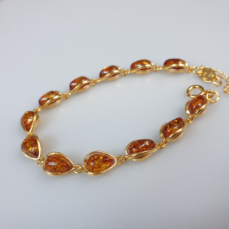 May include: A gold bracelet with amber teardrop-shaped stones. The bracelet has a delicate chain and a secure clasp.