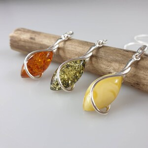 May include: Three amber pendants with silver twisted wire settings. The amber stones are a light yellow, a dark green, and a dark orange.