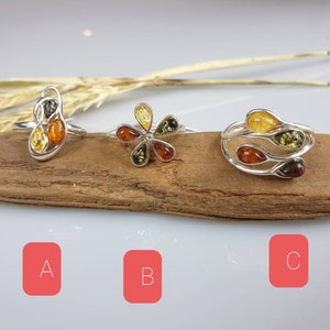 May include: Three silver rings with amber stones. The rings are on a piece of driftwood. The rings are labelled A, B, and C.