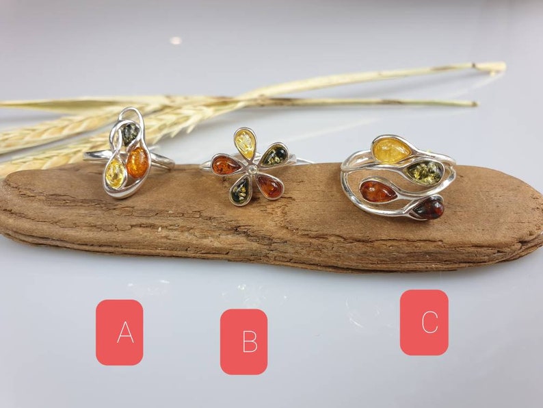 May include: Three silver rings with amber stones. The rings are on a piece of driftwood. The rings are labelled A, B, and C.