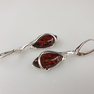 May include: A pair of silver dangle earrings with amber stones. The amber stones are a deep brown color and are set in a silver wire that wraps around the stone.