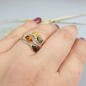 May include: A silver ring featuring three teardrop-shaped amber stones in shades of yellow, orange, and green.