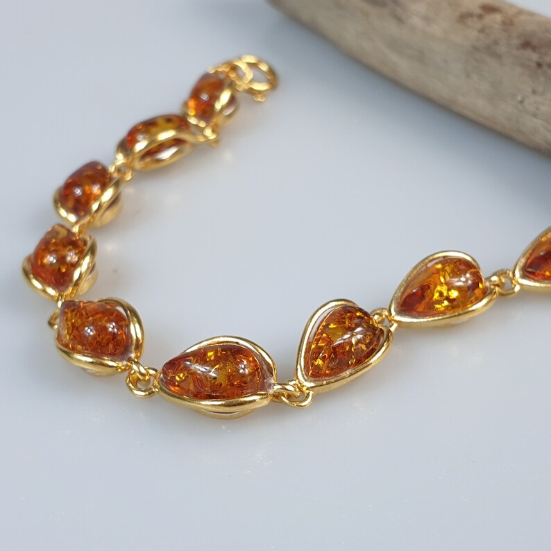 May include: A gold bracelet with amber teardrop-shaped stones. The bracelet is made of a delicate chain and has a simple clasp.