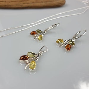 Op de afbeelding: Een zilveren ketting en oorbellen set met een hanger en oorbellen met drie amberstenen in tinten groen, geel en oranje.