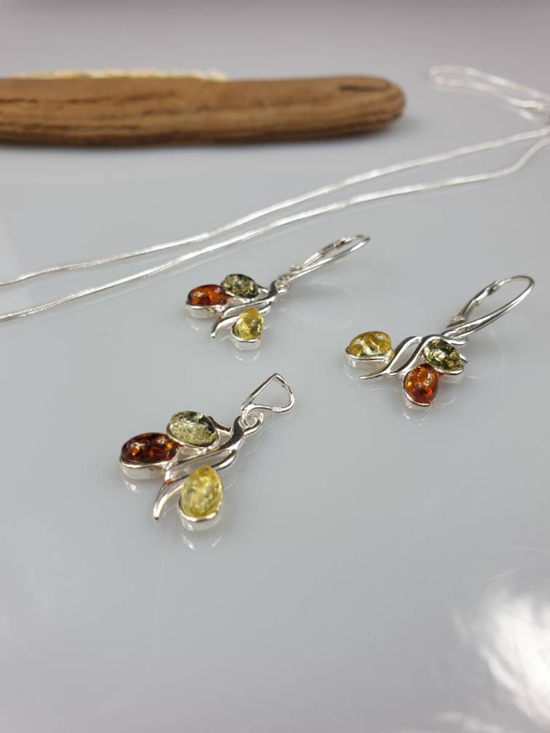 Op de afbeelding: Een zilveren ketting en oorbellen set met een hanger en oorbellen met drie amberstenen in tinten groen, geel en oranje.