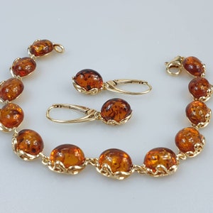 Könnte beinhalten: Ein goldfarbenes Armband und Ohrringe-Set mit Bernstein-Steinen. Das Armband hat ein Gliederketten-Design und die Ohrringe sind im Tropfen-Stil.